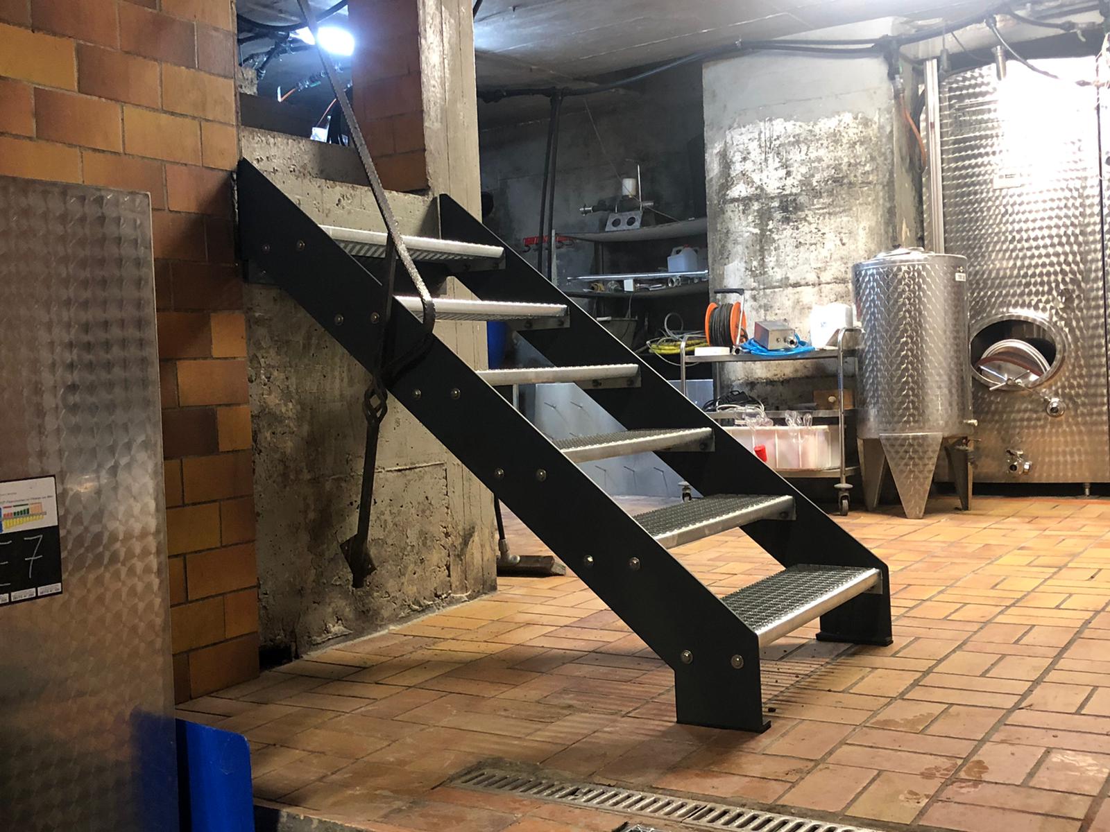 Schwarze Stahltreppe mit Gitterroststufen im Weinkeller zwischen Edelstahltanks