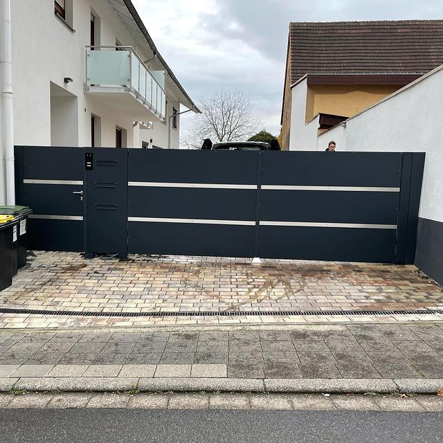 Anthrazitfarbenes Schiebetor mit Lamellenfüllung an einer Hofeinfahrt