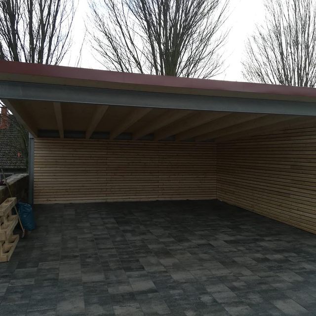 Carport mit Stahlrahmen und Holzverkleidung an einer gepflasterten Einfahrt